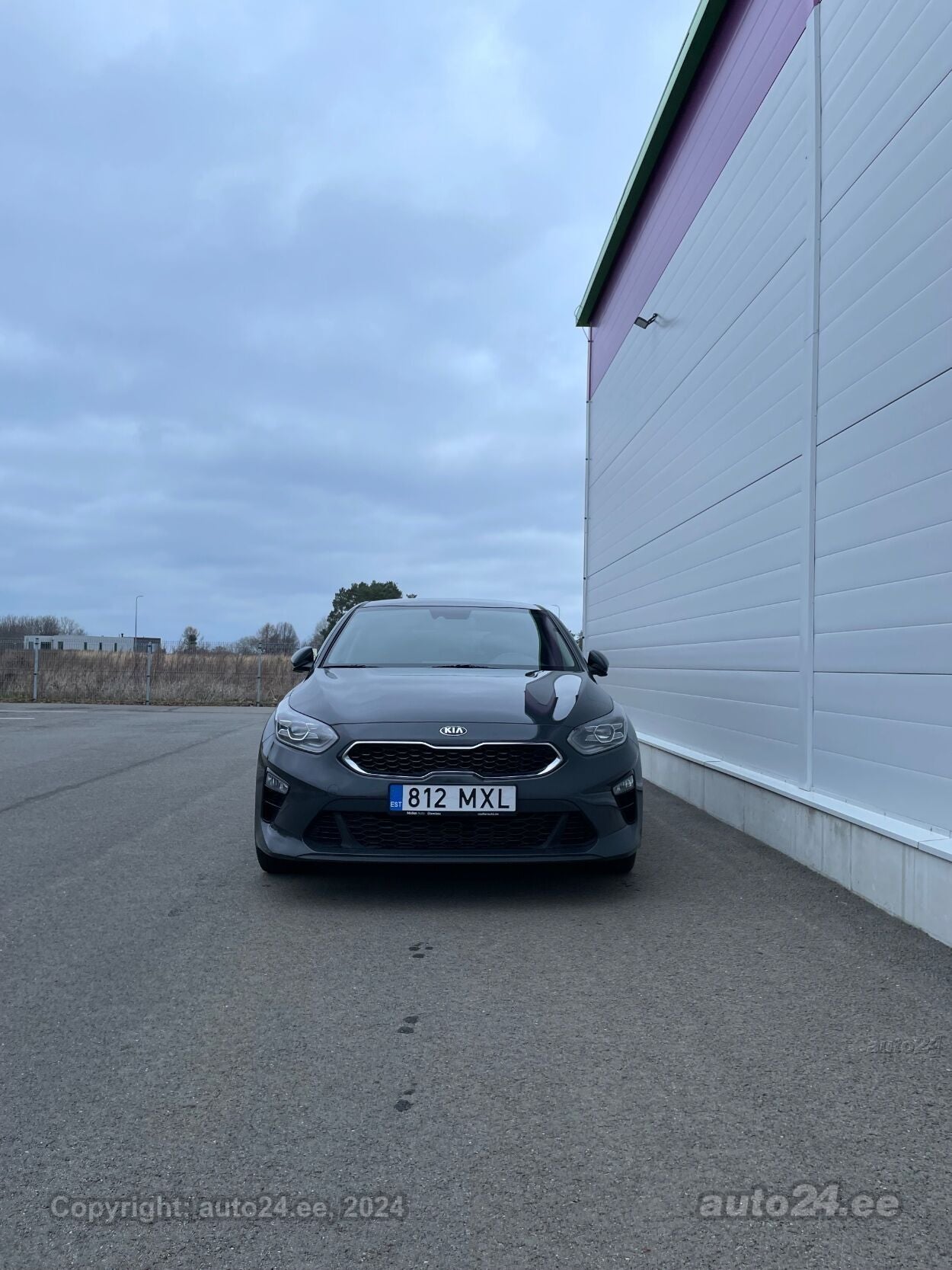 Gray Kia car parked beside a white industrial building under a cloudy sky, in an empty paved lot, file 192673636.jpg gallery 1