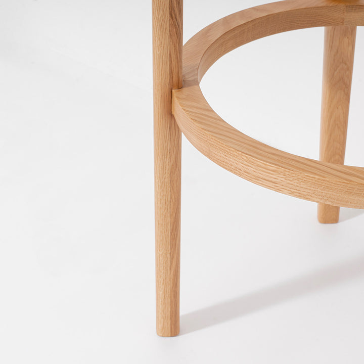 Close-up of a light natural oak wooden stool leg and curved circular ring support on a clean white background.
