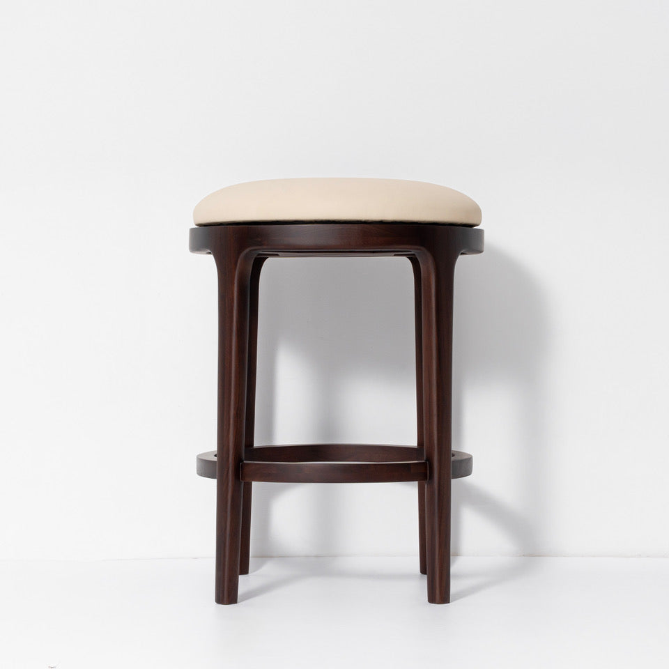 A modern bar stool with a dark brown wooden frame and a light beige upholstered seat cushion, shown against a plain white studio background.