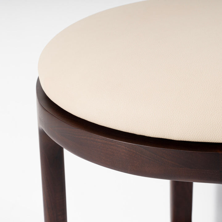 Close-up of a round upholstered stool or chair with a light cream seat cushion and a dark brown wooden frame, shown against a clean white background.