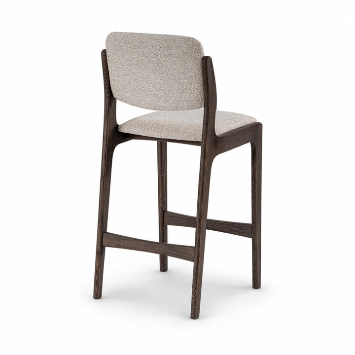 A modern bar stool with a dark brown wooden frame and a light beige textured fabric seat and backrest, shown from a three-quarter angle on a white background.