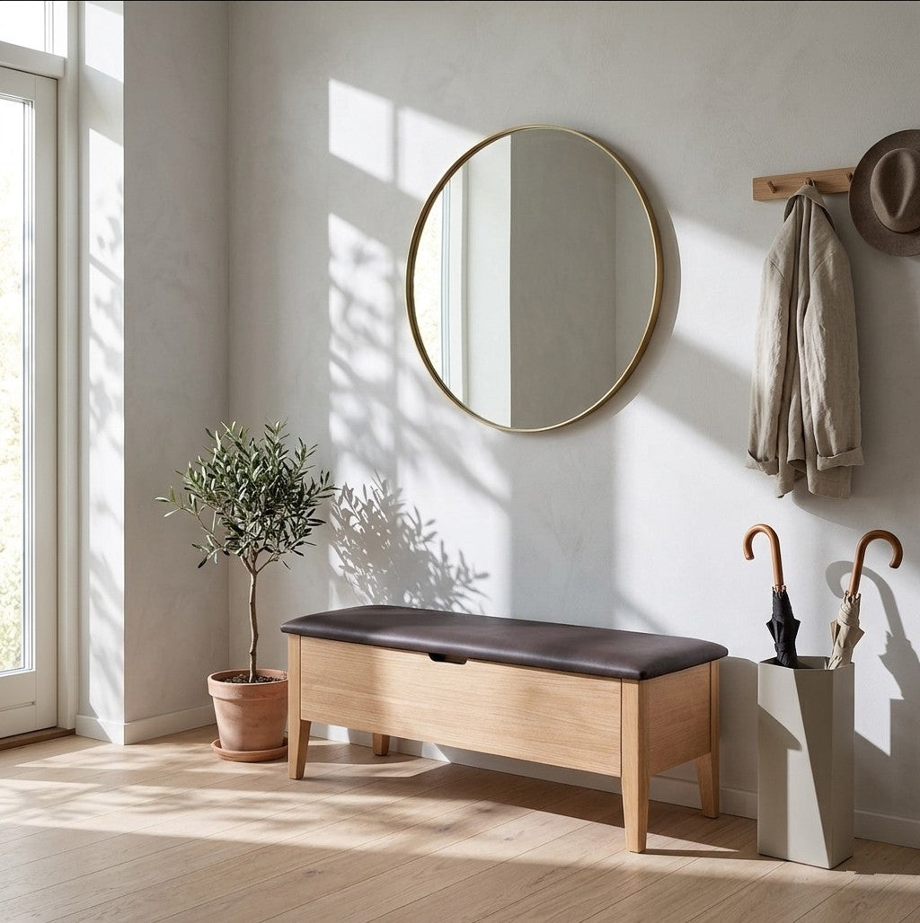 Wooden bench with a cushion, round mirror, plant, and coat in a well-lit room.