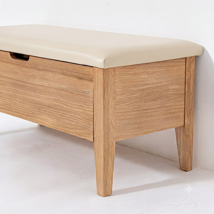 A wooden storage bench with a light beige upholstered top and a single drawer on the front, shown against a plain white wall and floor.