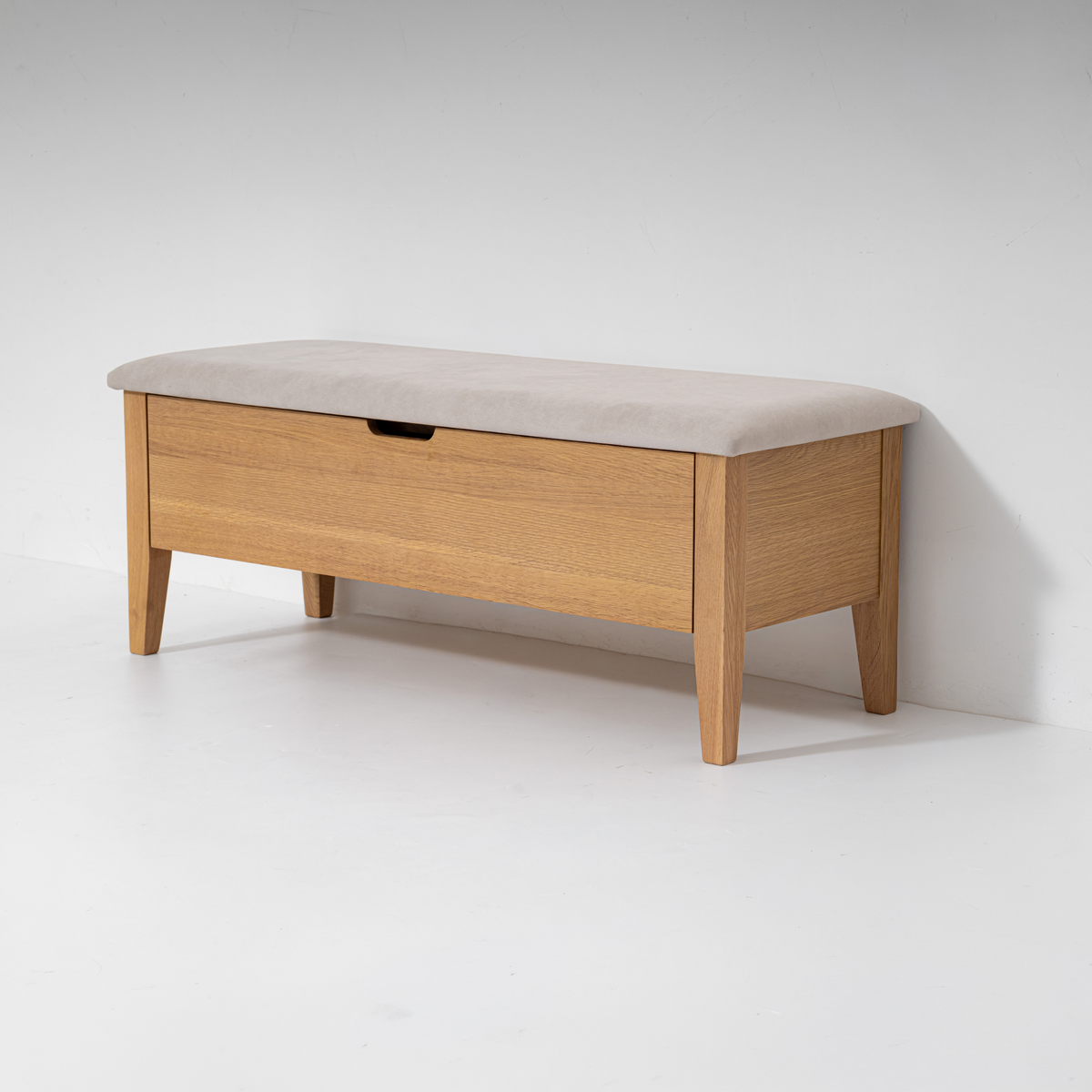 A light oak wood storage bench with a beige upholstered cushioned top and a single front drawer, photographed against a plain white studio background.