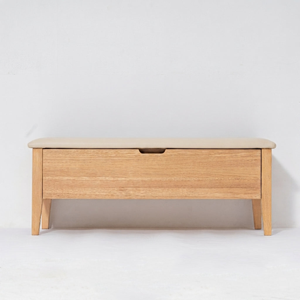 A light oak wood storage bench with a single drawer featuring a recessed pull handle, set against a plain white studio background.