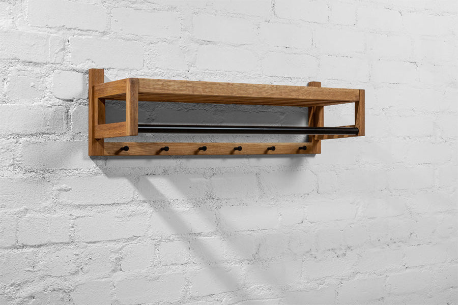 Solid oak coat rack with shelf and black hooks, used for hanging jackets, a scarf, and a stylish bag