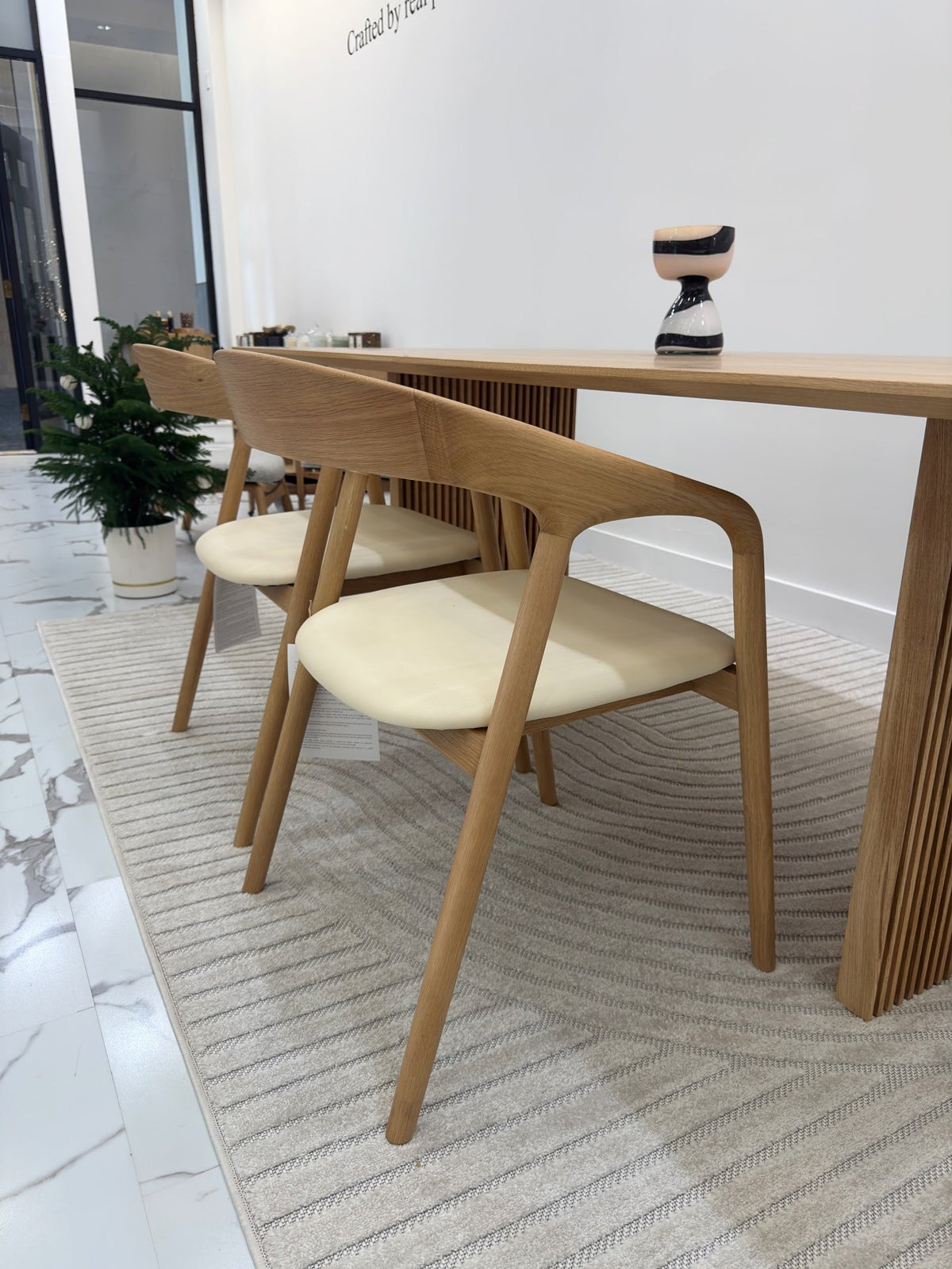 Two Celeste Oak Dining Chairs with beige leather seats tucked under a solid oak dining table in a designer showroom