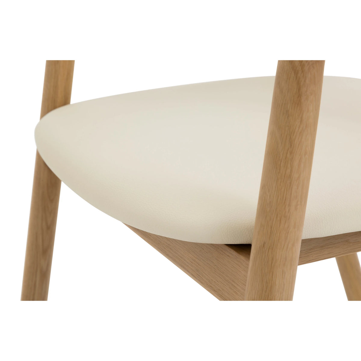 Close-up of Celeste Oak Dining Chair seat from behind showing smooth beige leather surface, rounded edge, and solid oak leg