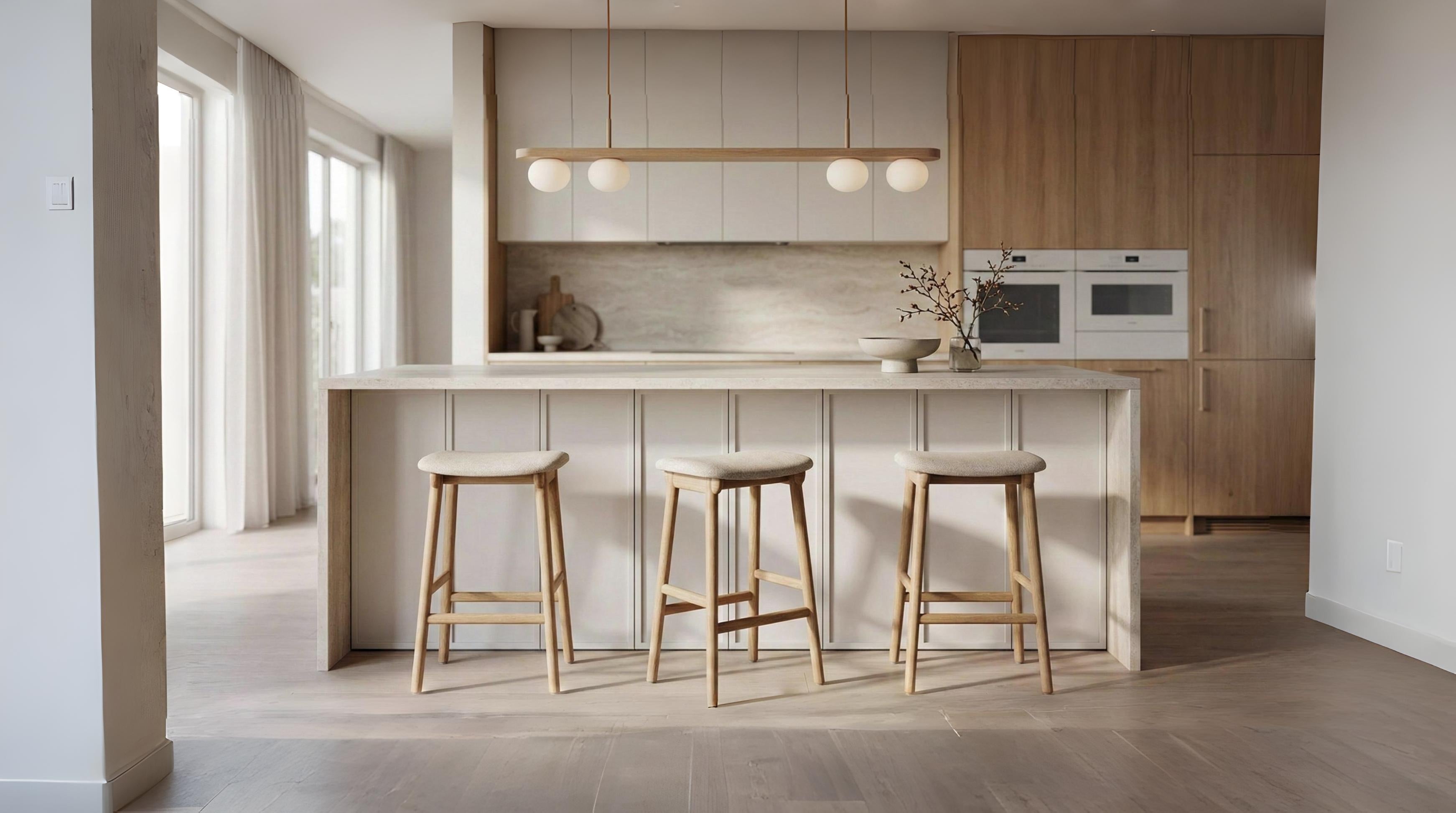 Modern kitchen interior with white island, three wooden stools, wood-paneled wall, built-in appliances, and soft natural lighting.