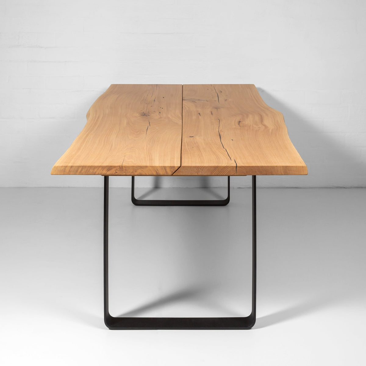 End view of the Oaken dining table showing the live edge oak top and black metal leg