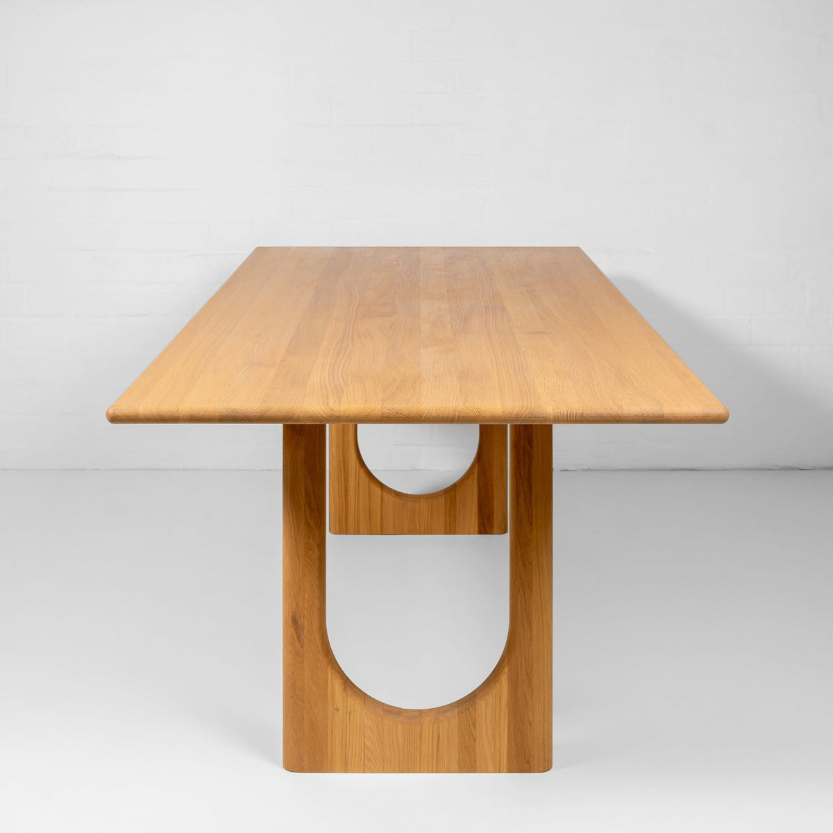 End view of the Theo oak dining table showing its sculptural U-shaped base