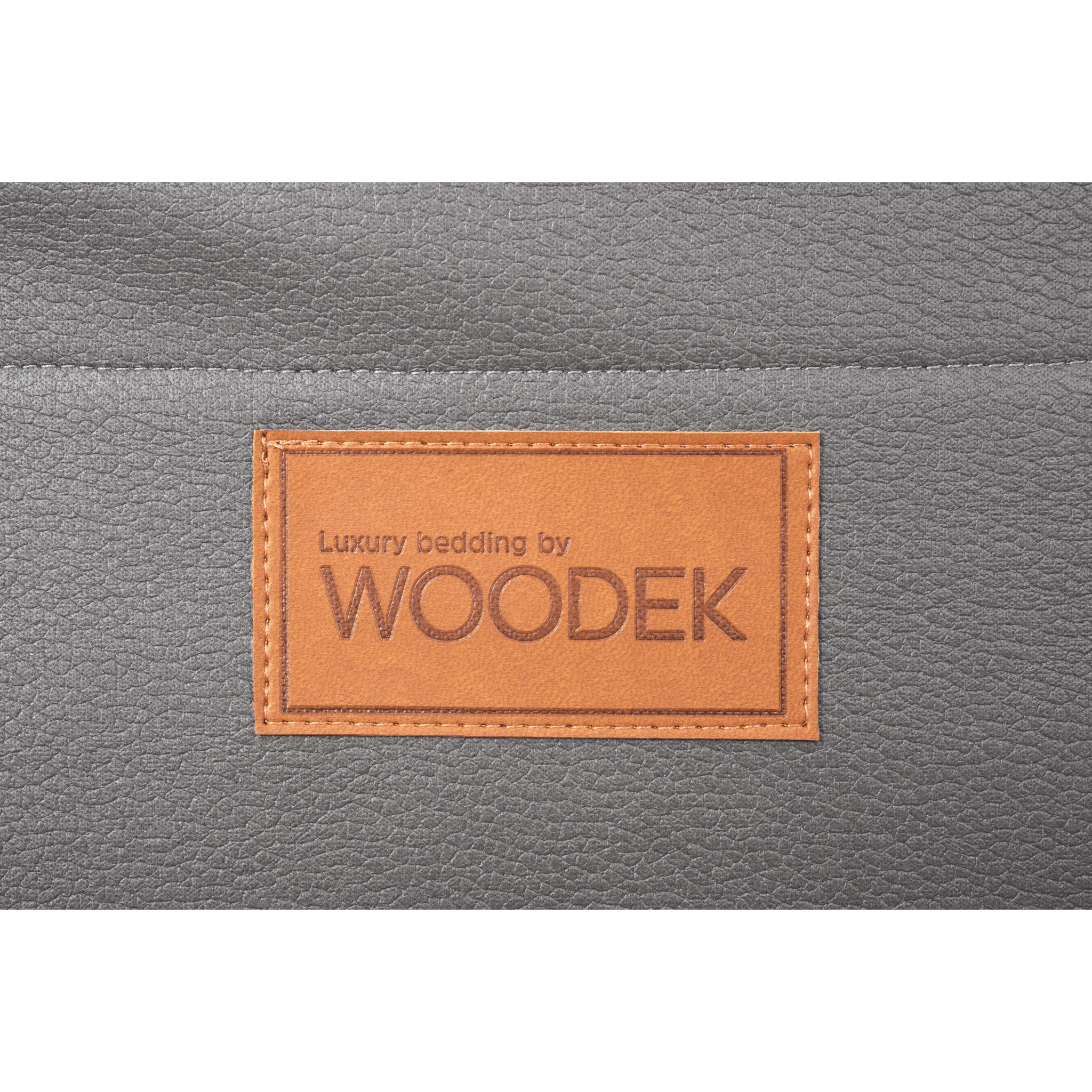 A brown leather patch reading "Luxury bedding by WOODEK" is stitched onto the grey fabric surface of the Woodek 2-in-1 Dog Travel Bag & Mattress, ideal as a portable dog bed for travel or home use.