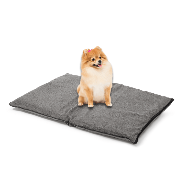 A small fluffy dog with a pink bow sits on the large, rectangular grey Woodek 2-in-1 Dog Travel Bag & Mattress against a white background.
