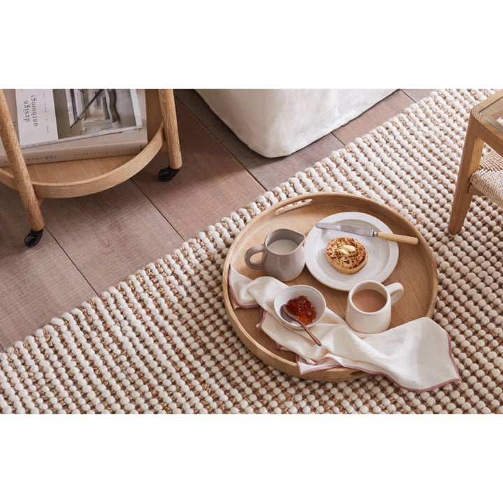 Wooden Serving Table Hugo - Walnut round tray on textured rug with ceramic cups, plate, and folded linen
